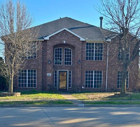 Two-story red brick home with two trees in the front yard.